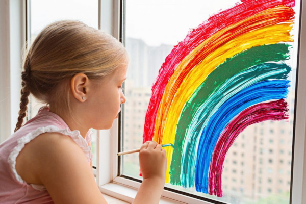 A young girl painting a rainbow on a window